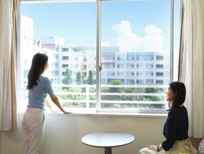 Dos personas en una habitación con un ventanal grande, una mesa redonda y vistas a edificios.