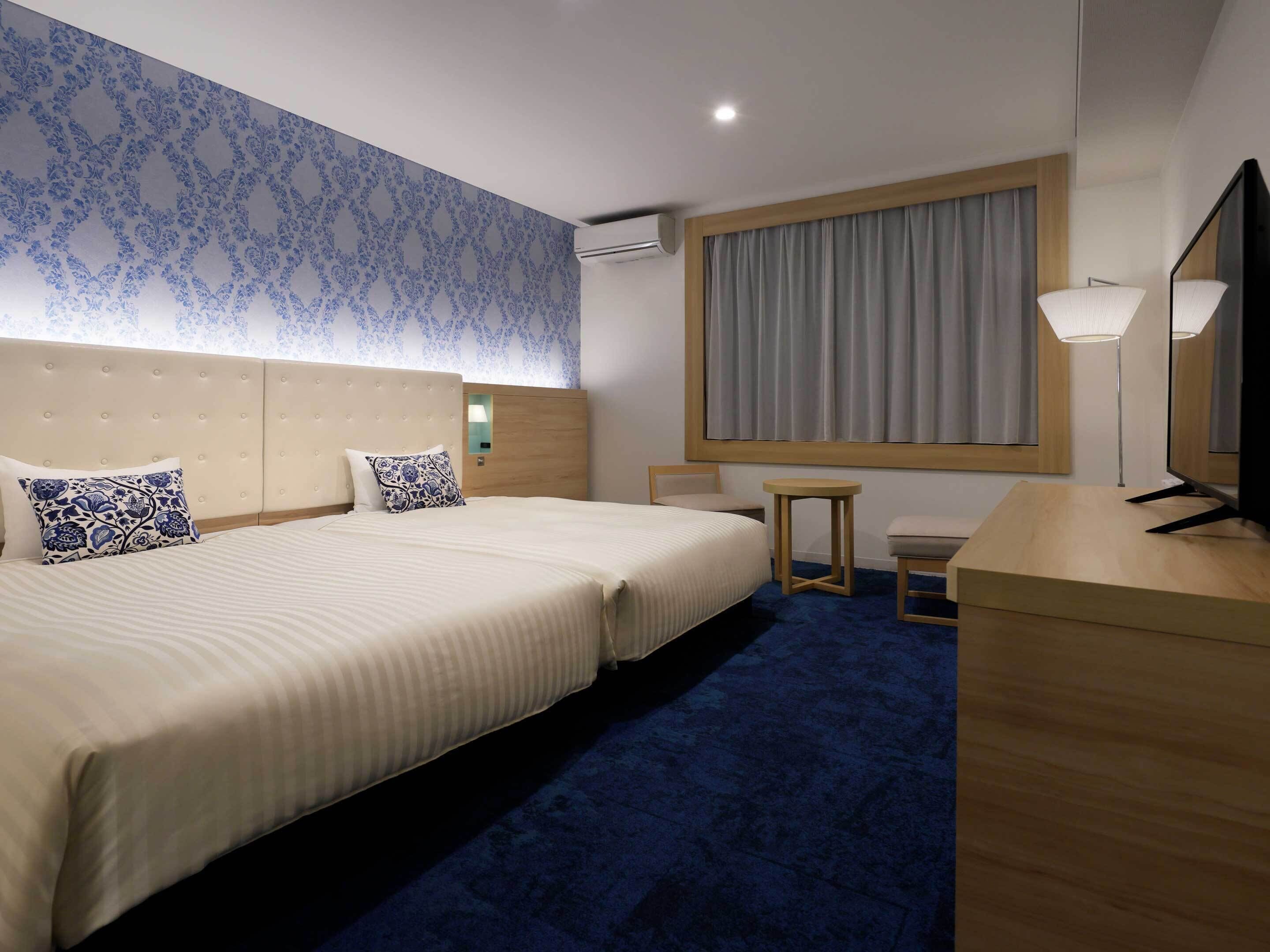 Habitación de hotel con una cama grande, un escritorio, una silla, una mesita, un espejo y una ventana con cortinas.
