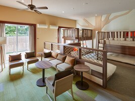 Una habitación de hotel con balcón, un conjunto de sofás, dos mesas redondas y un ventilador de techo.