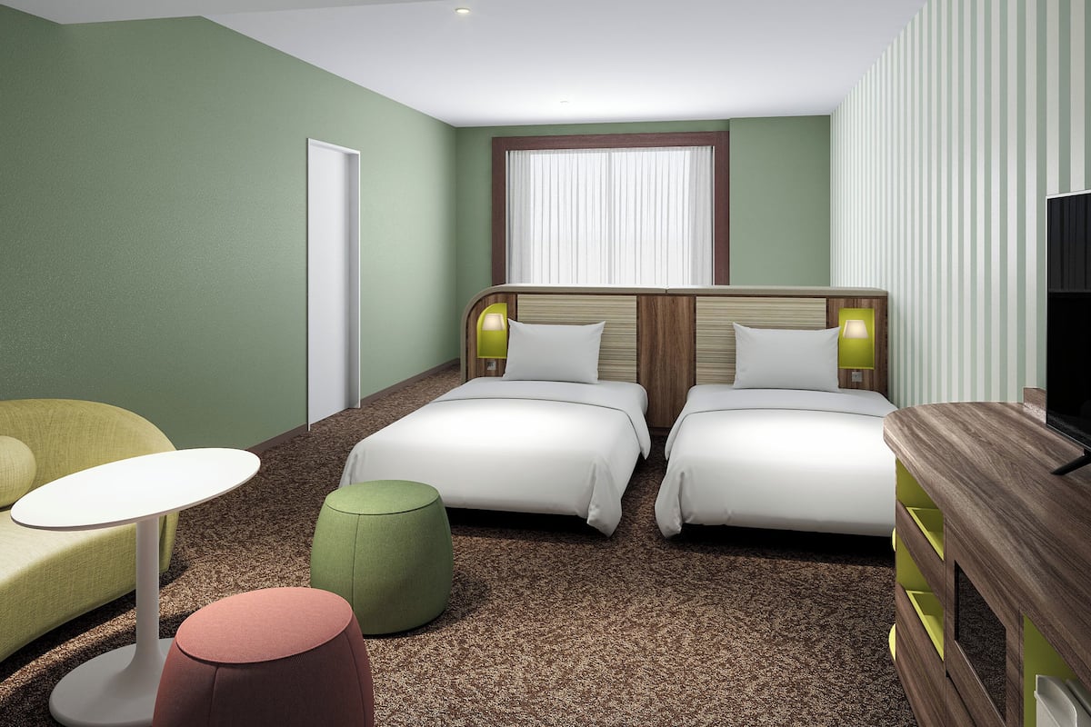 Ein Hotelzimmer mit zwei Betten, einem Fernseher, einem kleinen Tisch und einem grünen Hocker.