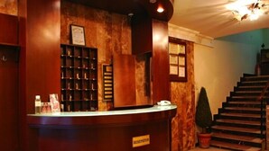 A reception desk with a sign reading "RECEPTION" in a hotel lobby with a marble wall, a staircase, and a potted plant.