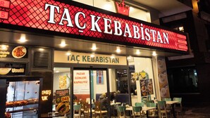 A restaurant named 'TACKEBABISTAN' with a glass facade, outdoor seating, and a sign with a crown symbol.