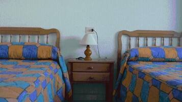 Una habitación con dos camas, cada una con una colcha estampada, una mesita de noche con una lámpara y un cajón.