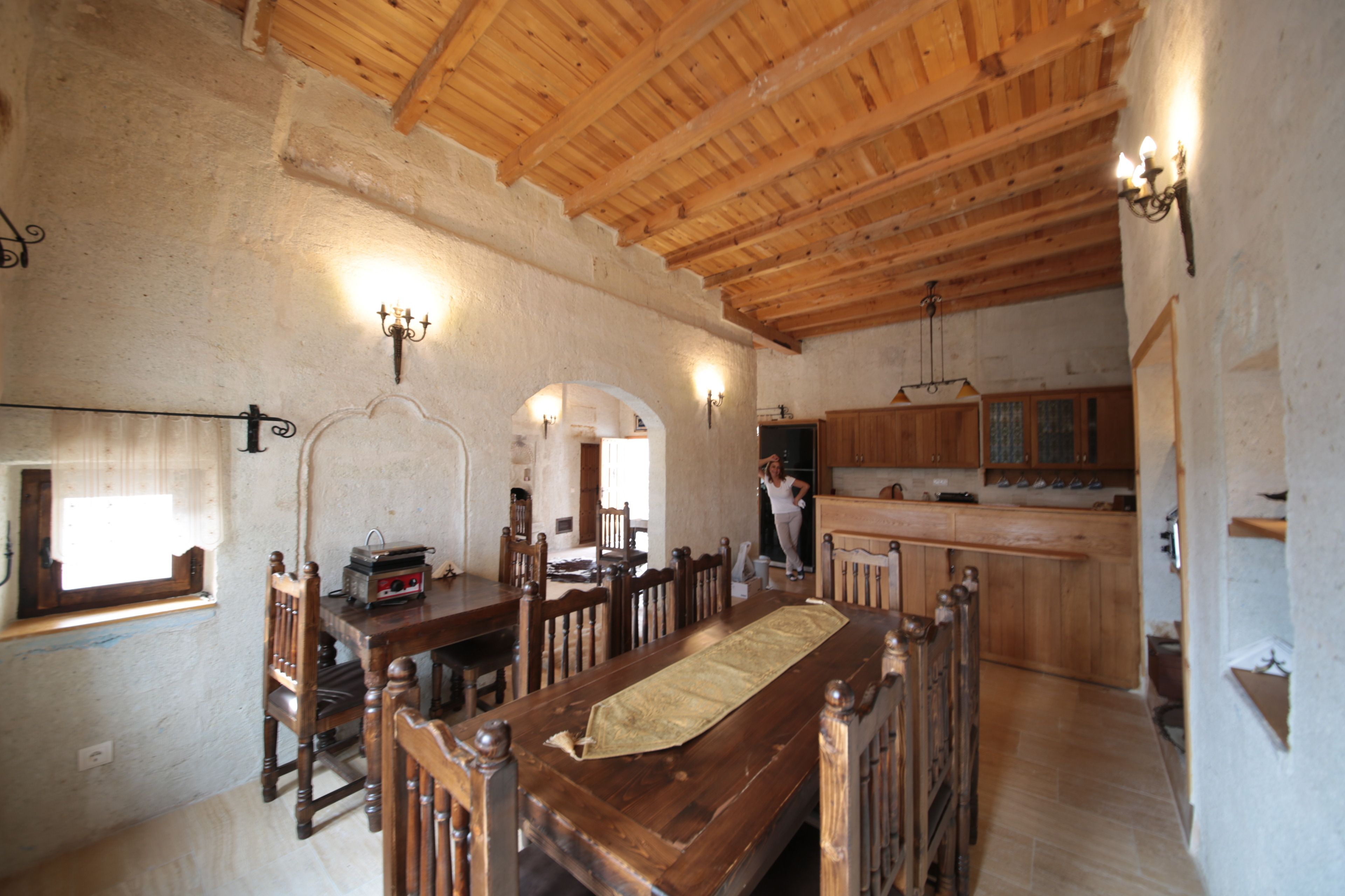 A rustic dining area with wooden furniture, a long table, and a kitchen in the background.