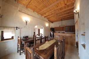 A rustic dining area with wooden furniture, a long table, and a kitchen in the background.
