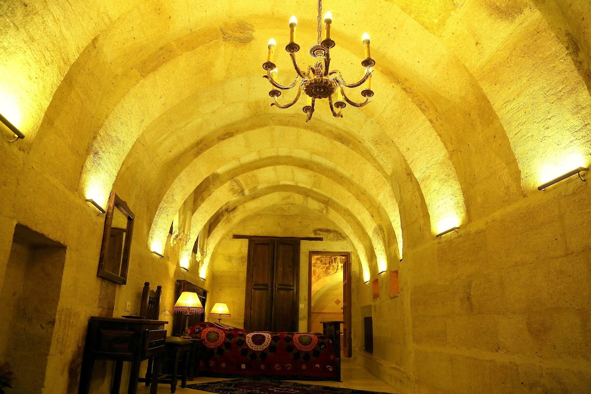 An arched hallway with a chandelier, wooden doors, and a patterned rug.