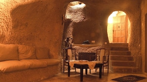A cozy room with a stone wall, a wooden door, a sofa, a table, and a staircase. - Hanımkız Konagi (Avanos)