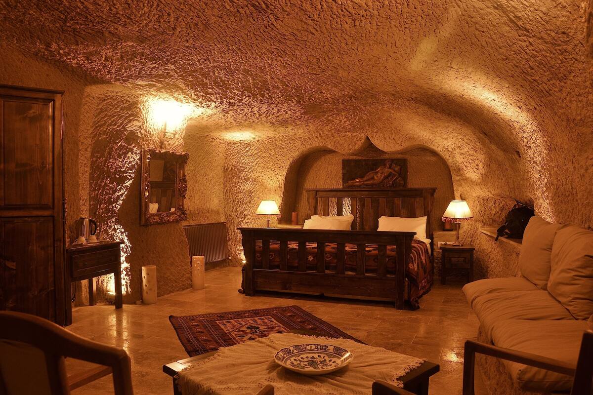 A cozy, rustic room with a vaulted ceiling, a wooden bed, a sofa, and a dining table with a plate.
