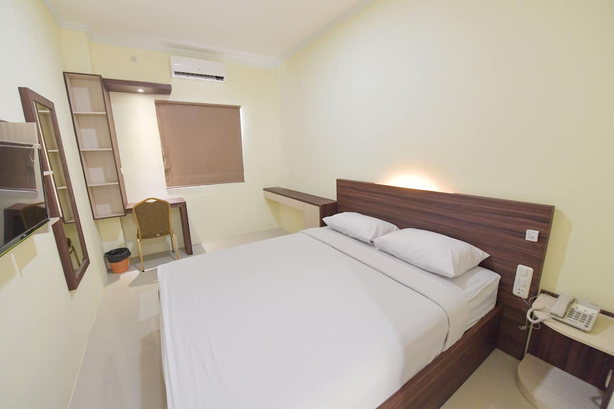A neatly arranged hotel room with a large bed, a bedside table with a phone, a chair, a small desk, and a wardrobe.