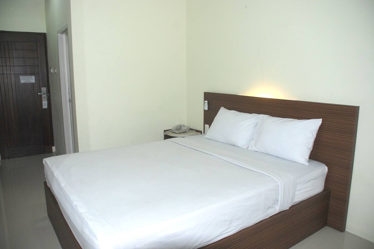 A neatly made bed with white linens in a room with a wooden headboard and a nightstand with a telephone.