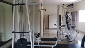 Et fitnessrum med forskellige træningsmaskiner, en bænk og en dør i baggrunden.