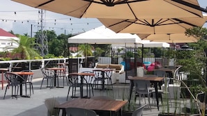 Un patio al aire libre con mesas y sillas, cubierto por sombrillas grandes, rodeado de vegetación.