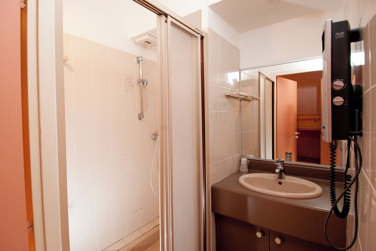 A bathroom with a shower, sink, and a telephone mounted on the wall.
