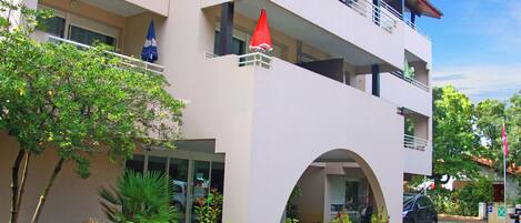 Un edificio de varios pisos con un arco de entrada central, balcones y plantas en macetas.