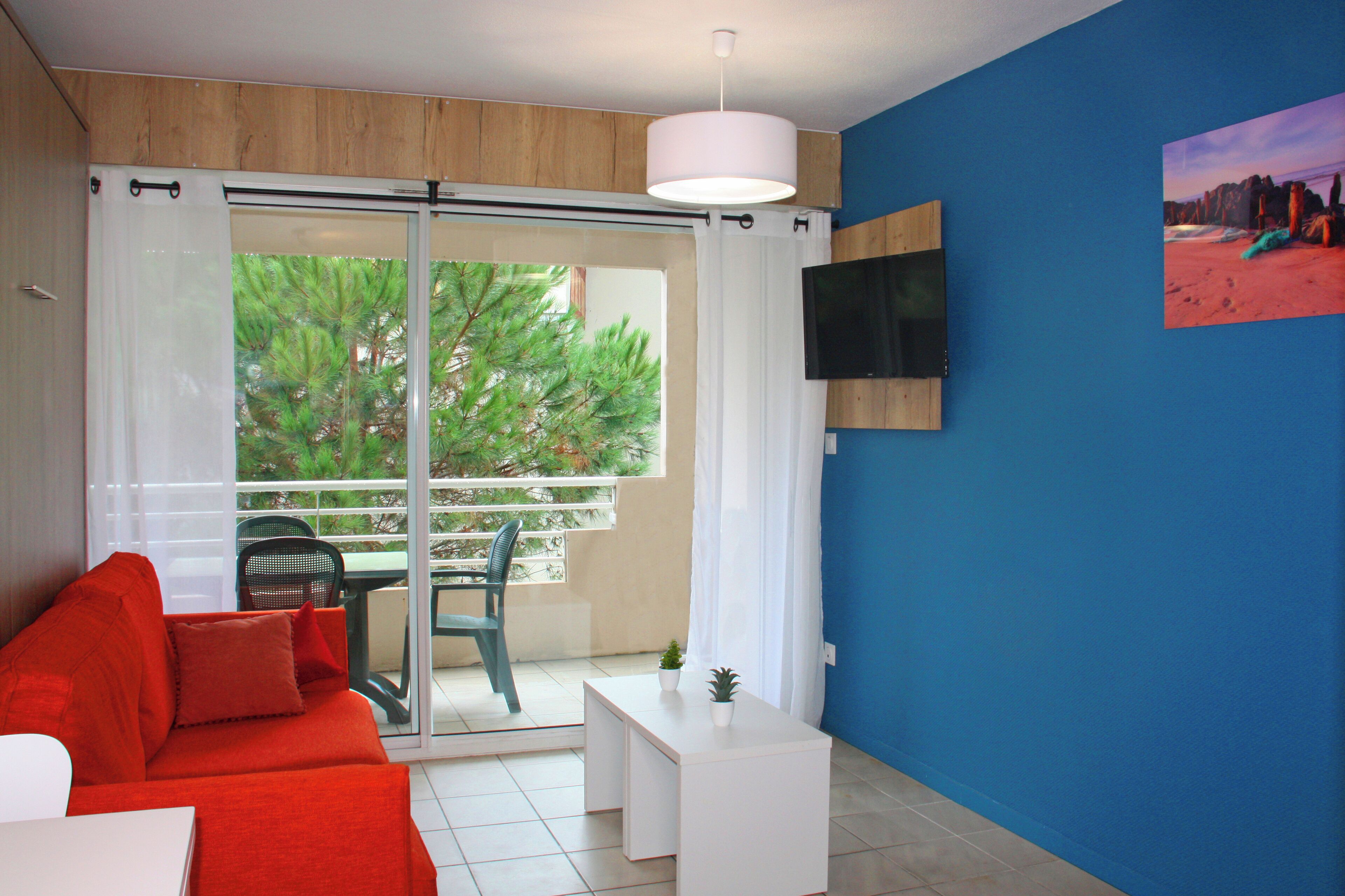 A modern living room with a red sofa, a white coffee table, and a TV mounted on a blue wall.