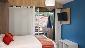 Un dormitorio con cama, almohadas rojas, un televisor en la pared y vistas a un edificio.
