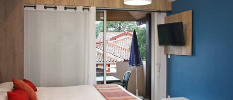 Un dormitorio con cama, almohadas rojas, un televisor en la pared y vistas a un edificio.
