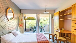 Un dormitorio con cama, un armario de madera, una mesita con silla y un balcón con mesa y sillas.