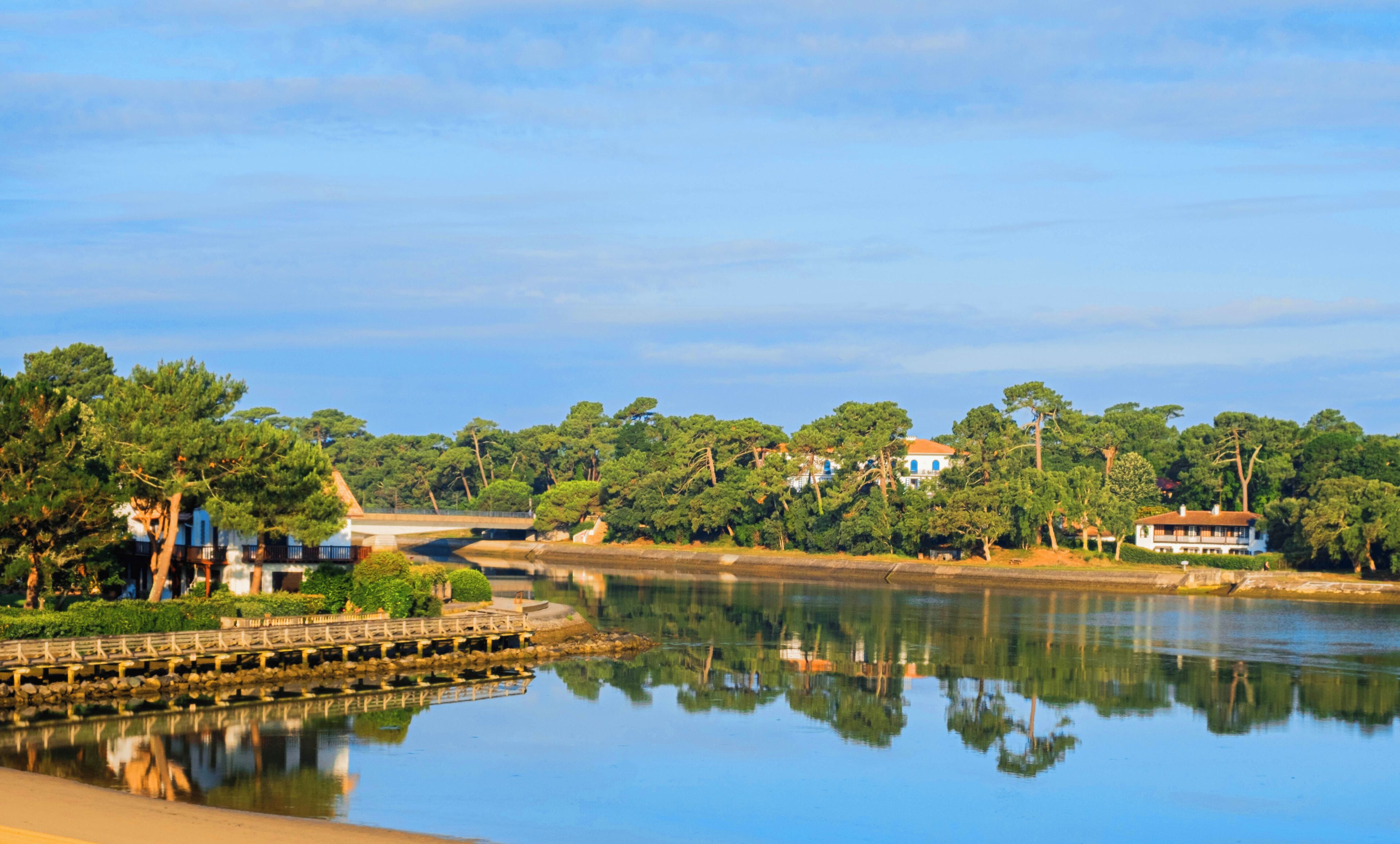 A calm river with a bridge, surrounded by lush greenery and buildings.