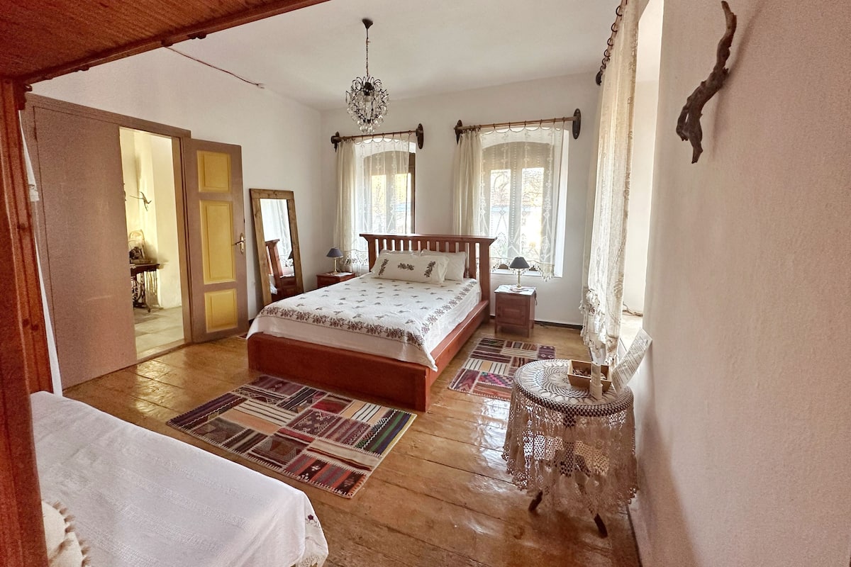 Un dormitorio amplio con una cama grande, piso de madera, candelabro y vistas al exterior.