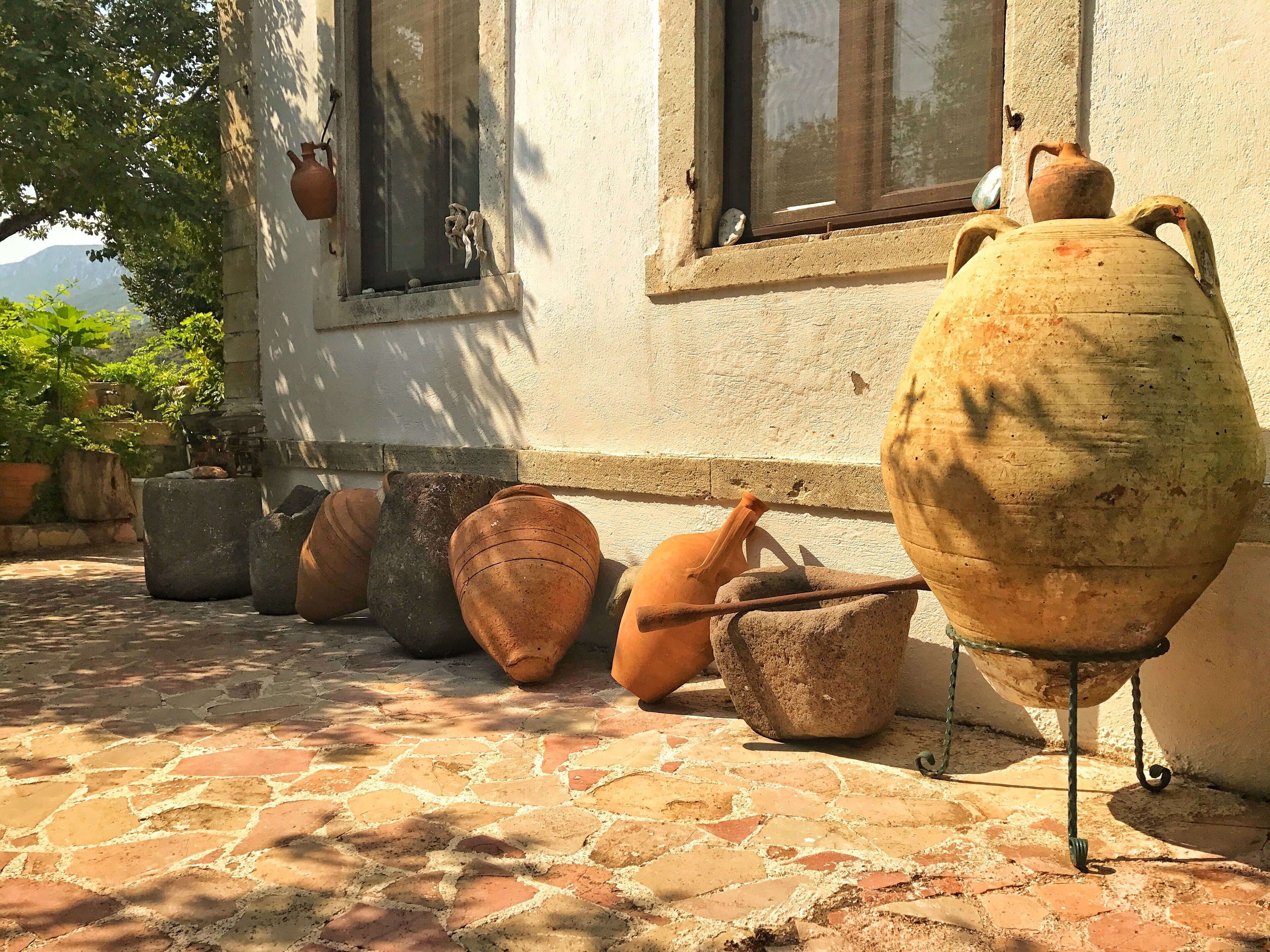 Terracotta pots and a large ceramic pot on a stone-paved patio next to a building with windows.