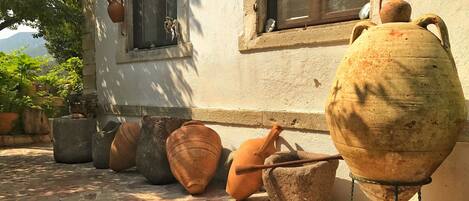 Terracotta pots and a large ceramic pot on a stone-paved patio next to a building with windows.
