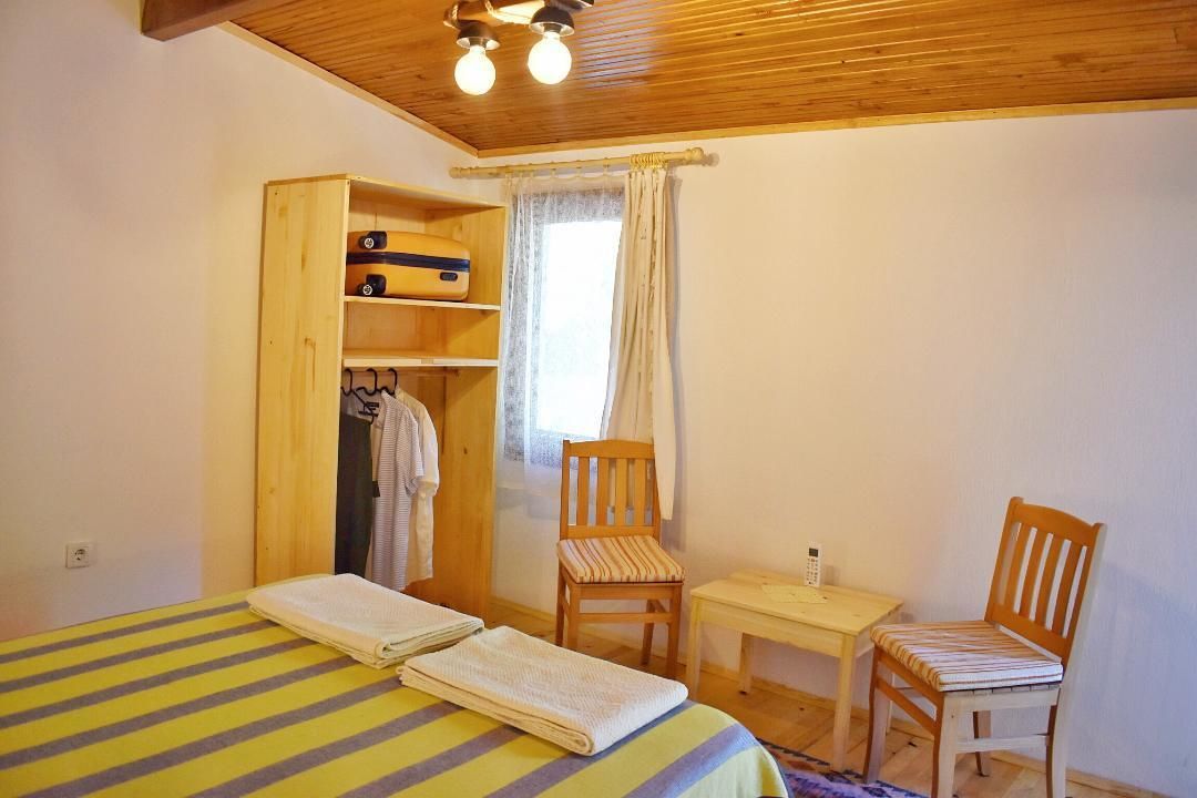 Una stanza con un letto, due sedie, un tavolino, un armadio in legno e una finestra con tende.