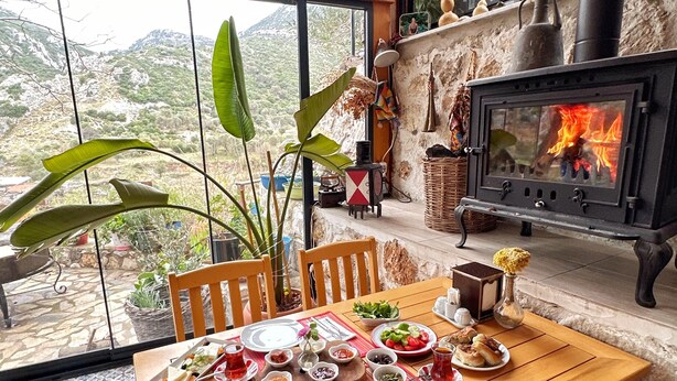 A dining area with a table set for a meal, a fireplace, and a view of the outdoors. - Saklı Konak (Karaburun)