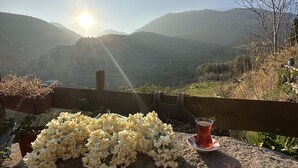 A stone bench with a bouquet of white flowers and a glass of red drink, overlooking a mountainous landscape with the sun shining. - Saklı Konak (Karaburun)