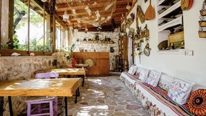 A rustic interior with stone flooring, wooden furniture, and various decorative items on shelves and walls. - Saklı Konak (Karaburun)