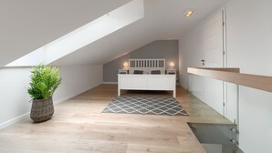 Een moderne slaapkamer met schuine wanden, een wit bed, bedlampen, een kamerplant en een kamerbreed tapijt met patroon.