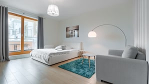 Een moderne slaapkamer met een bed, een grijze bank, een klein tafeltje en een groot raam met gordijnen.