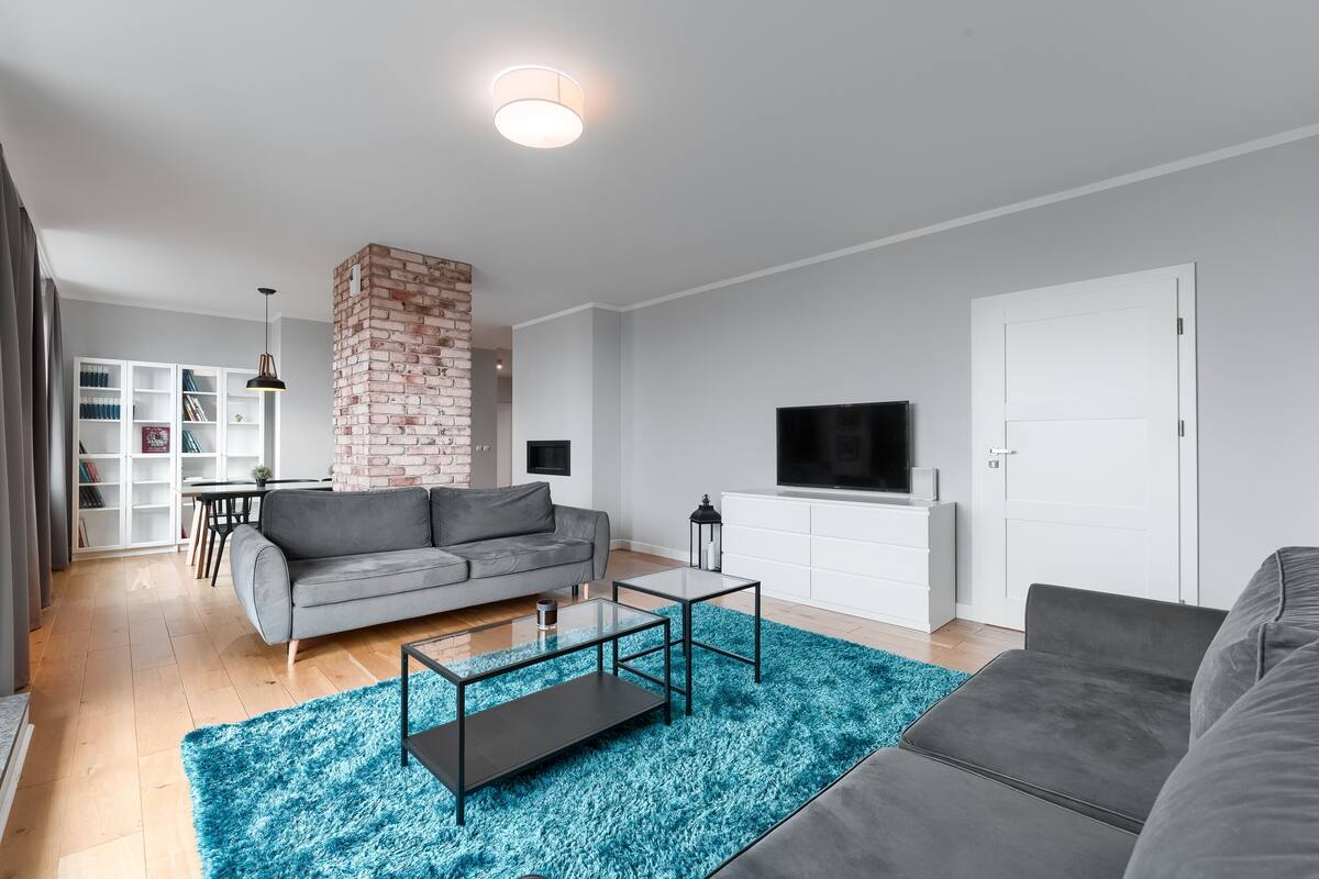Un salon moderne avec un canapé gris, une table basse, un téléviseur et un mur décoratif en briques.