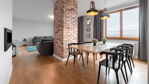 Een moderne woonkamer met een schouw van baksteen, een eettafel met stoelen, een bank en een groot raam met gordijnen.