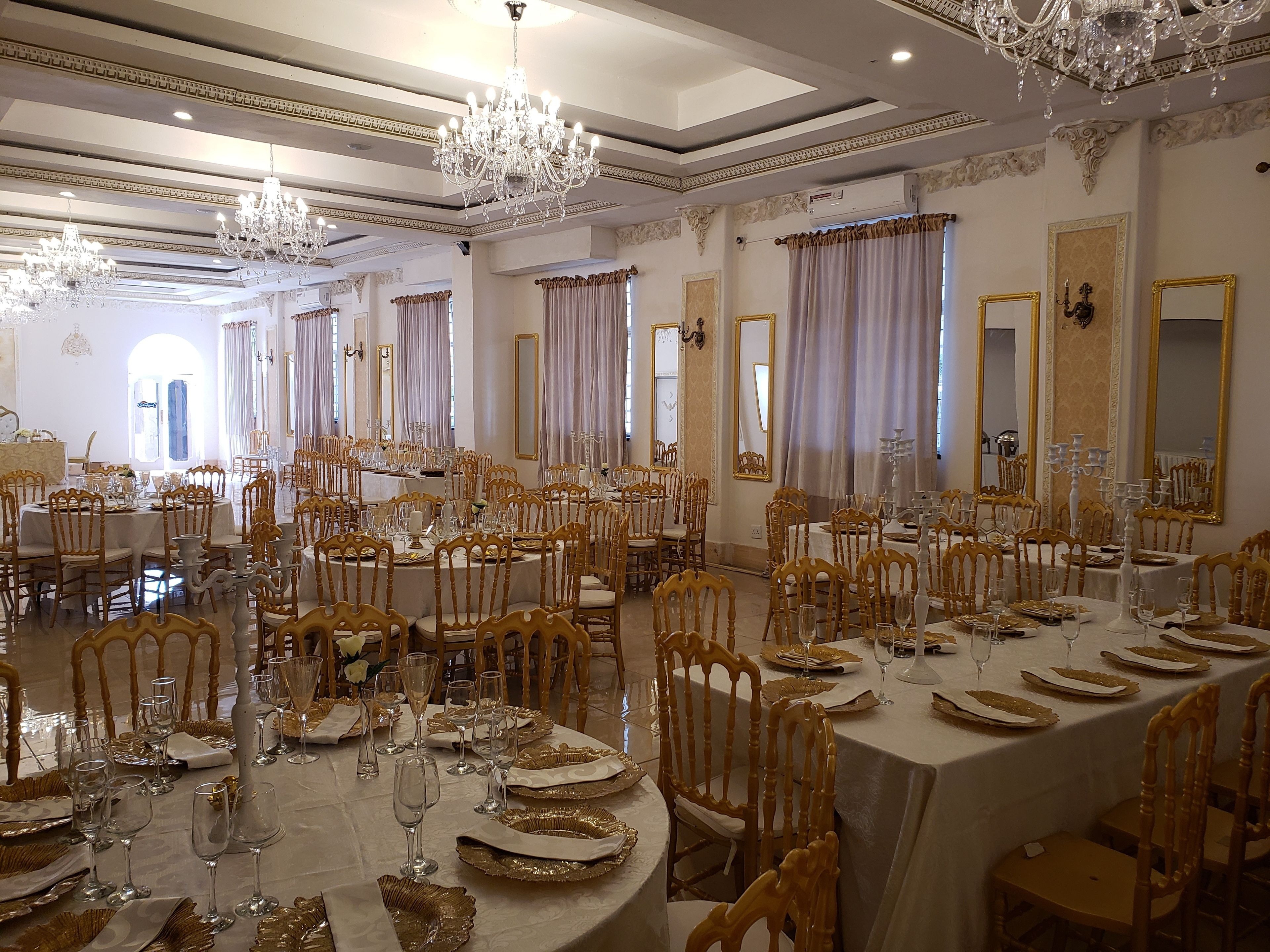 A grand banquet hall with ornate chandeliers, gold-framed mirrors, and elegantly set tables.