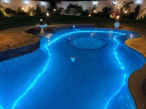 A swimming pool with blue LED lighting, a stone border, and a small fountain. - Selborne Hotel (Bulawayo)