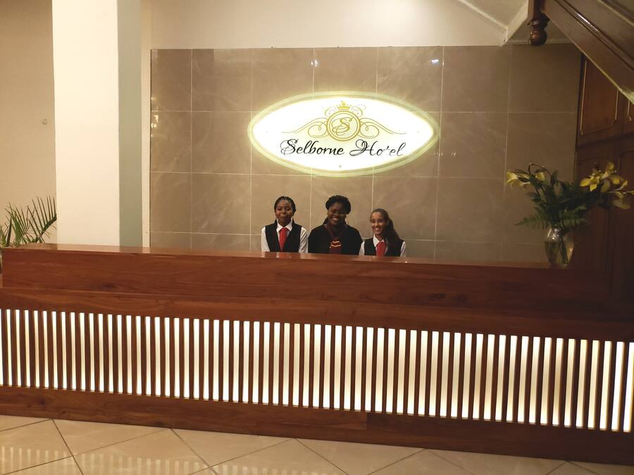 A reception desk at Selborne Hotel with a modern design, a logo above the desk, and a potted plant to the right.