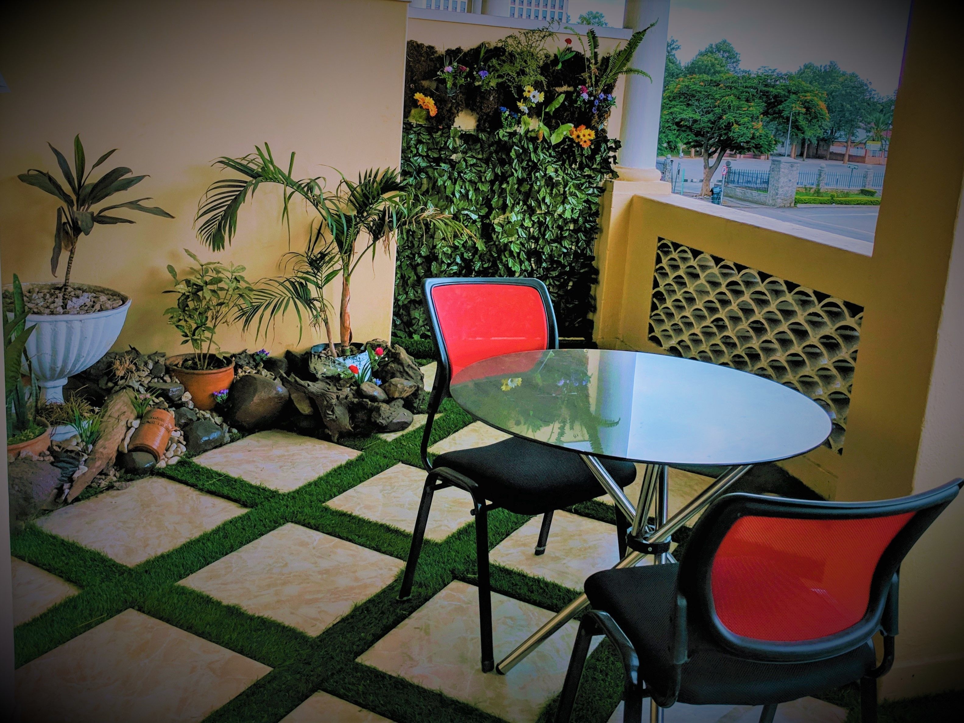 A patio area with a glass table, two chairs, potted plants, and a decorative wall.