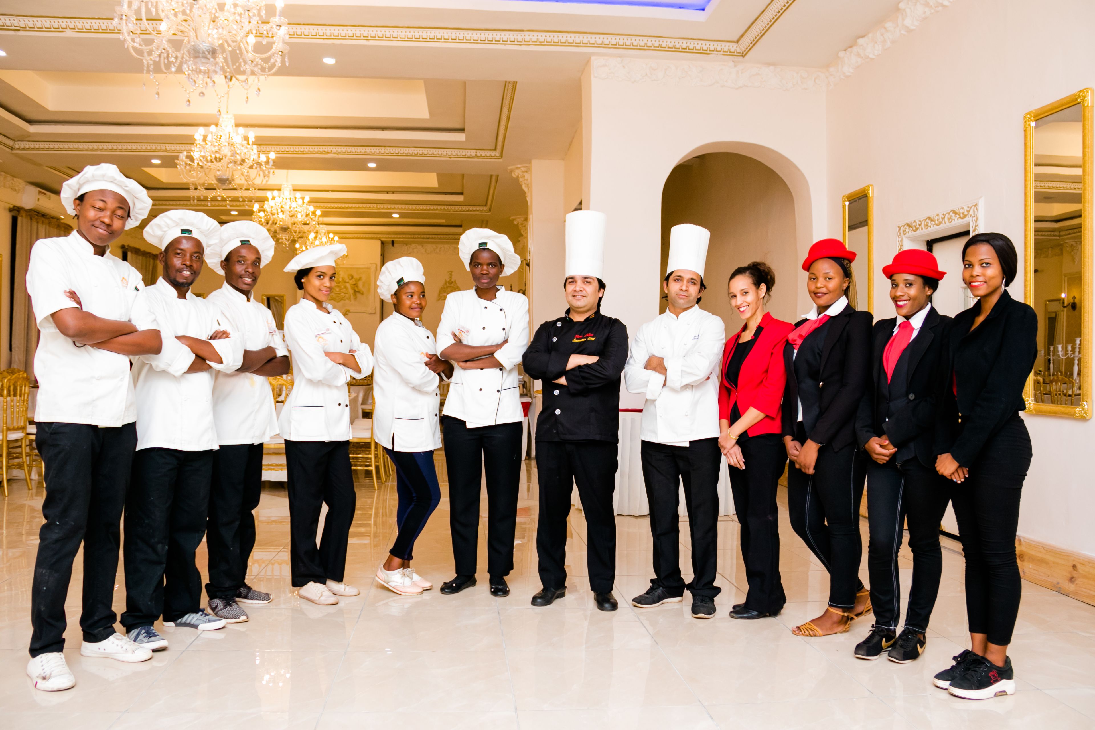 Un grupo de personas con vestimenta formal, algunas con gorros de chef, en una sala bien iluminada con candelabro y espejos con marcos dorados.