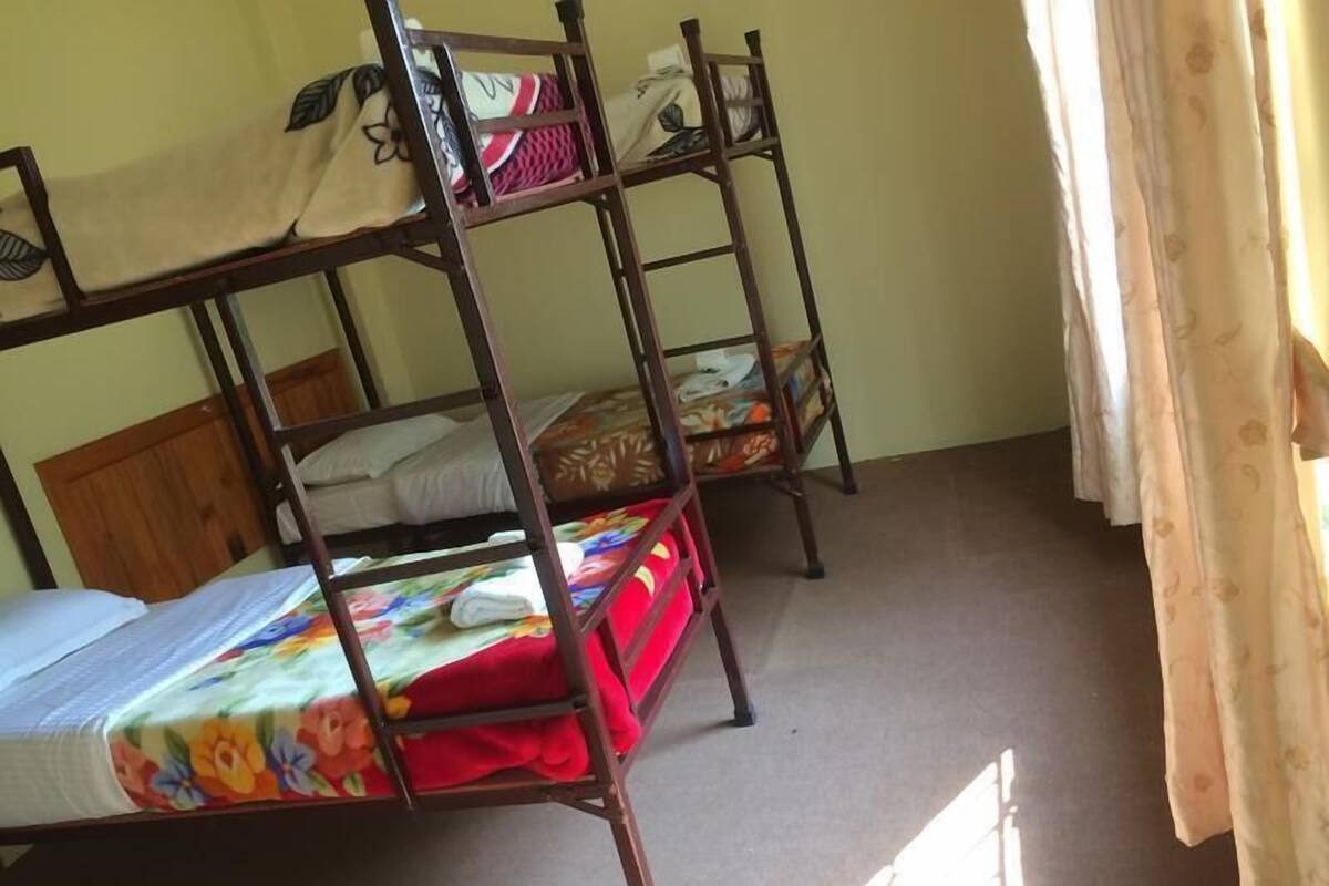 A dormitory room with bunk beds, a wooden headboard, and a window with curtains.