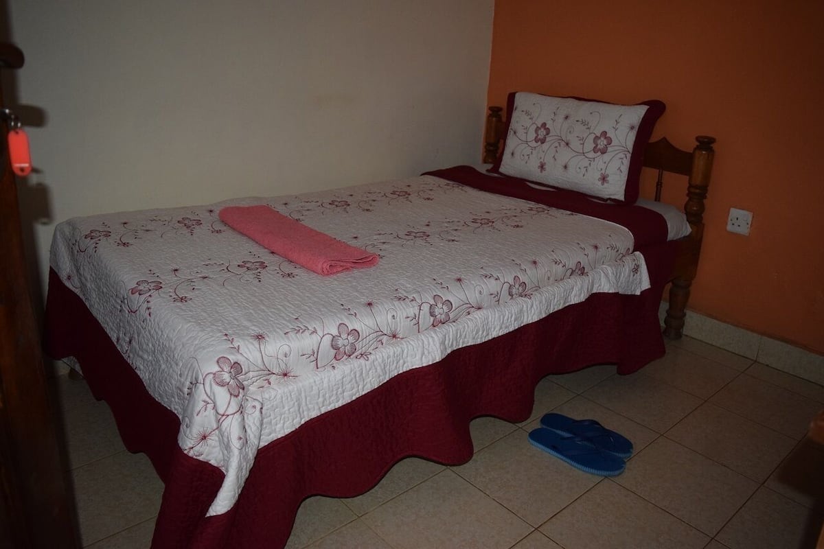 A single bed with a floral bedspread and a red skirted base. A pink towel is folded on the bed.