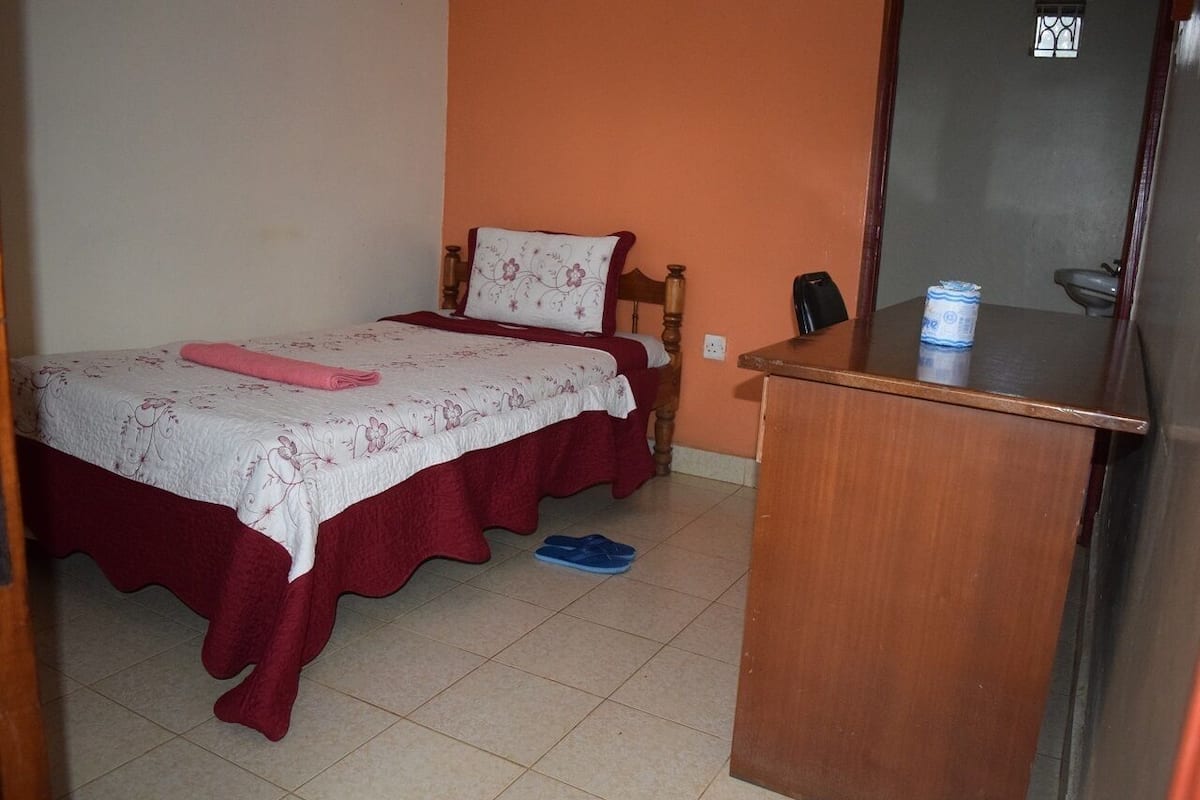 A bedroom with two beds, a wooden desk, and a bathroom visible through an open door.