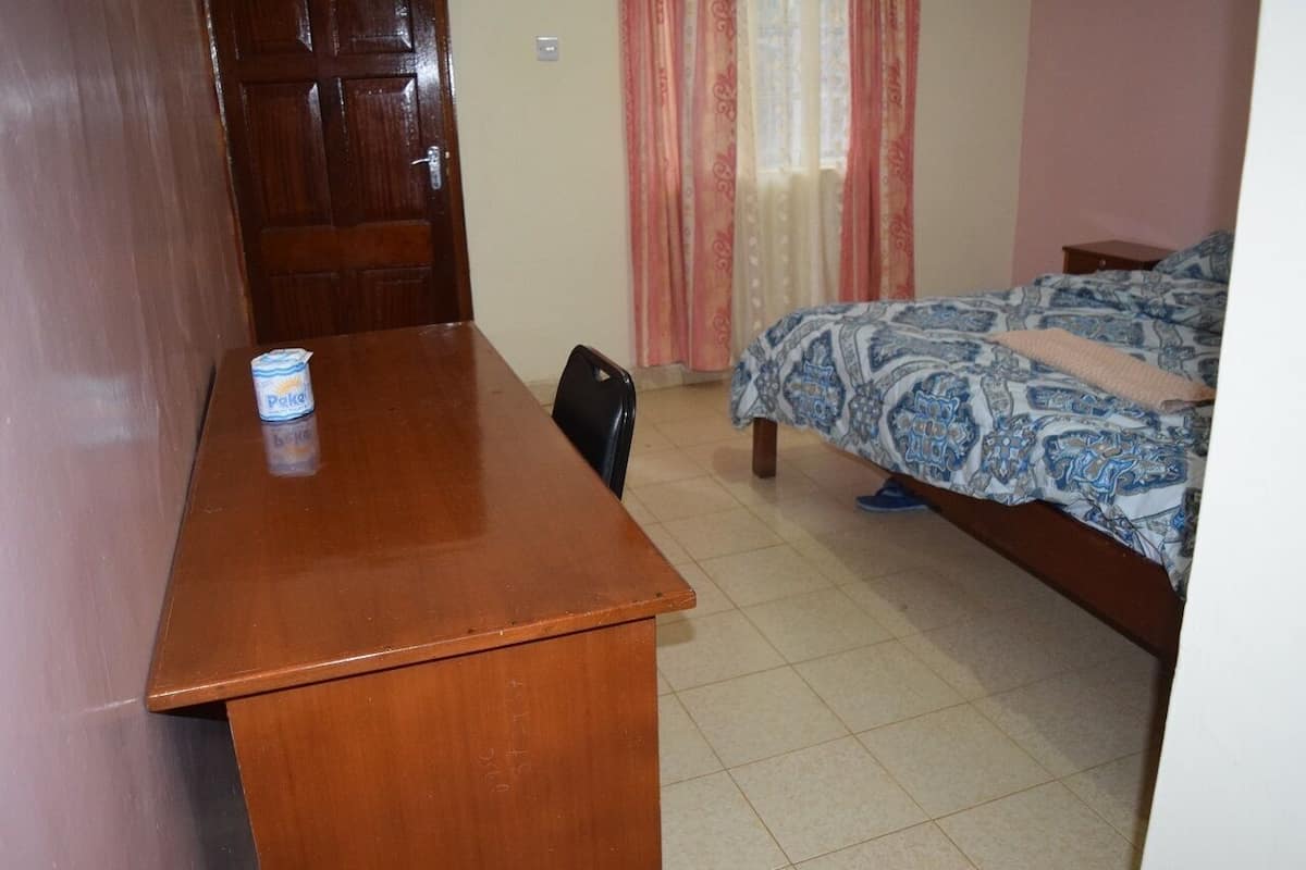 A room with a wooden desk, a bed with patterned bedding, a chair, and a curtain.