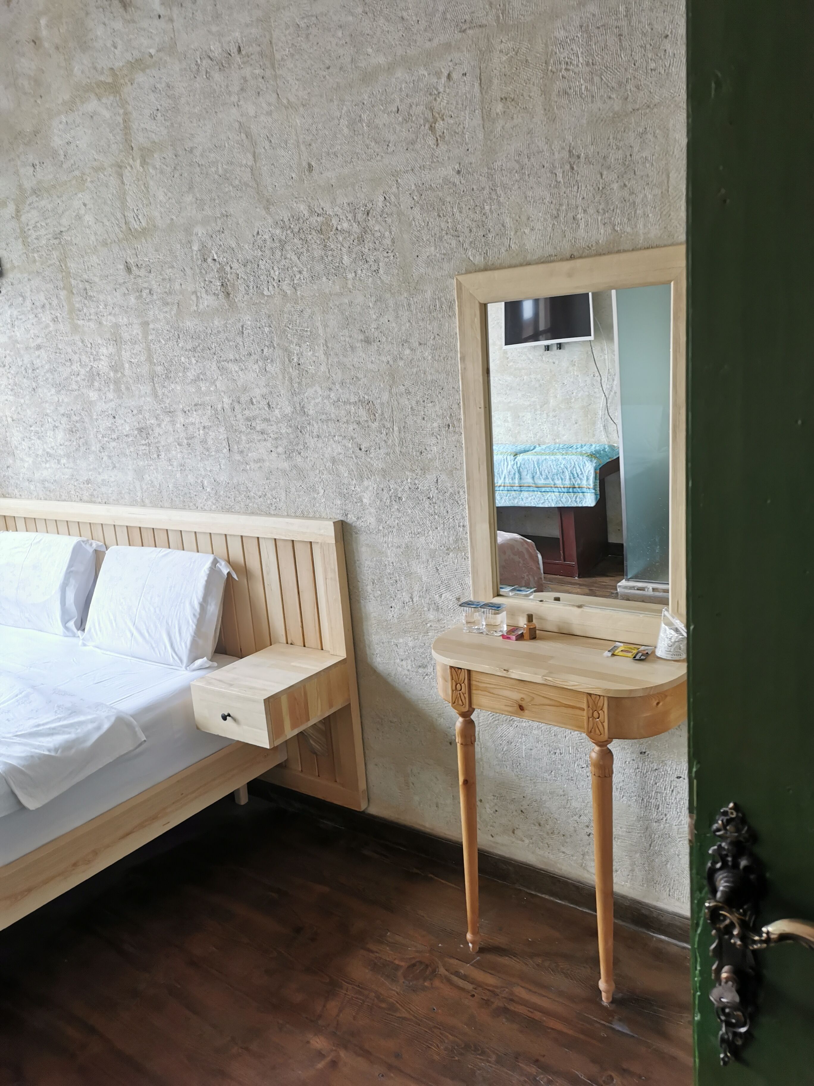 A bedroom with a wooden bed, a bedside table with toiletries, and a mirror on the wall.