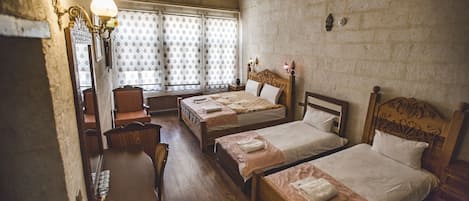 Una habitación tradicional con dos camas individuales, un escritorio de madera y un ventanal con cortinas estampadas.
