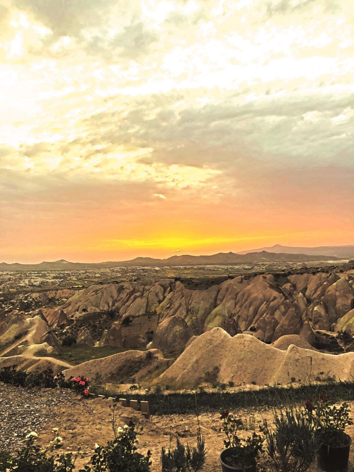 A panoramic view of a desert landscape with a sunset, featuring rugged terrain and sparse vegetation.