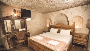 A wooden bed with a headboard, a wooden desk with a chair, a television mounted on the wall, and a wooden nightstand with a lamp. - House of Cappadocia (Ürgüp)