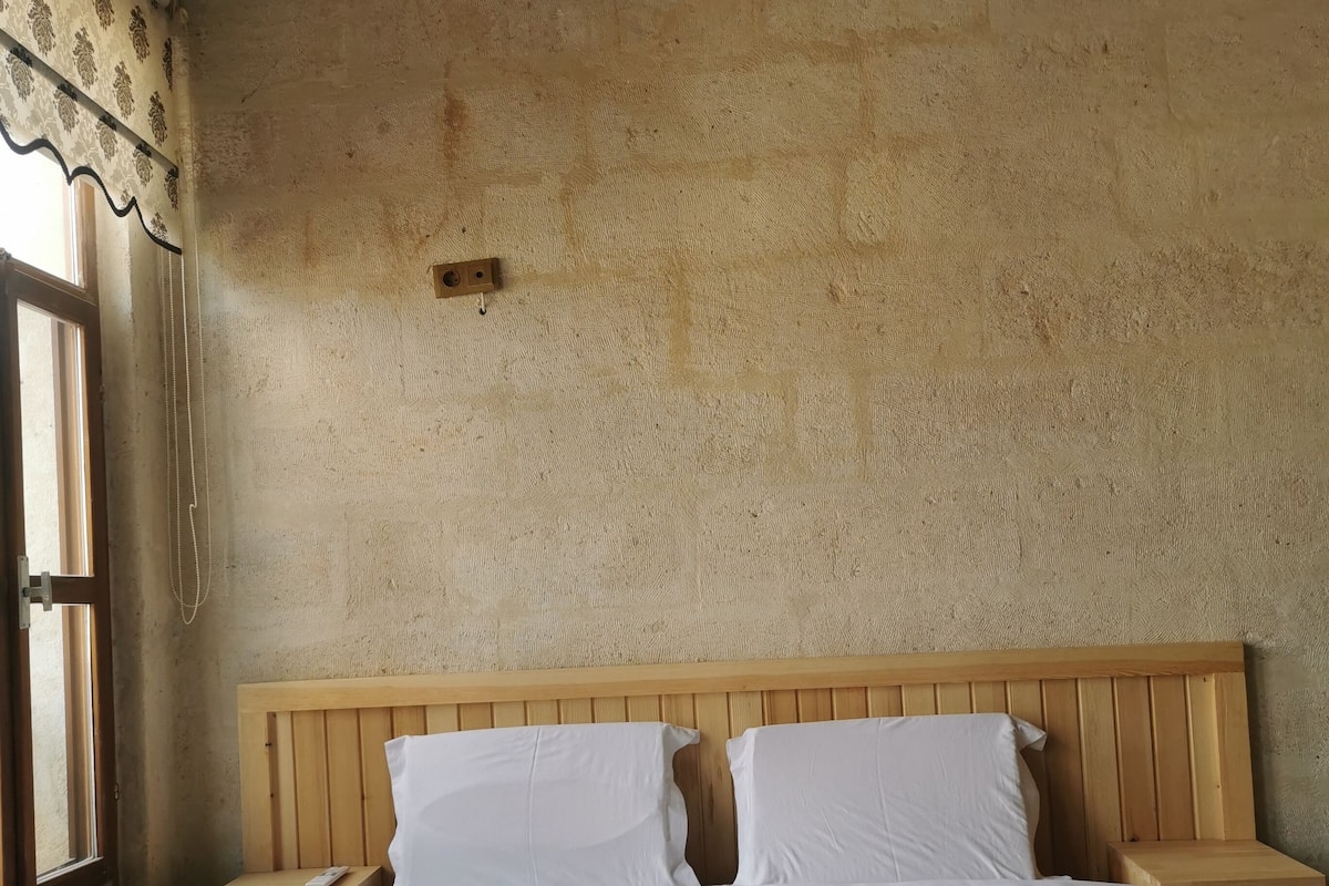 A bed with a wooden headboard, white linens, and a pink patterned bedspread. There are two bedside tables with a wooden finish.