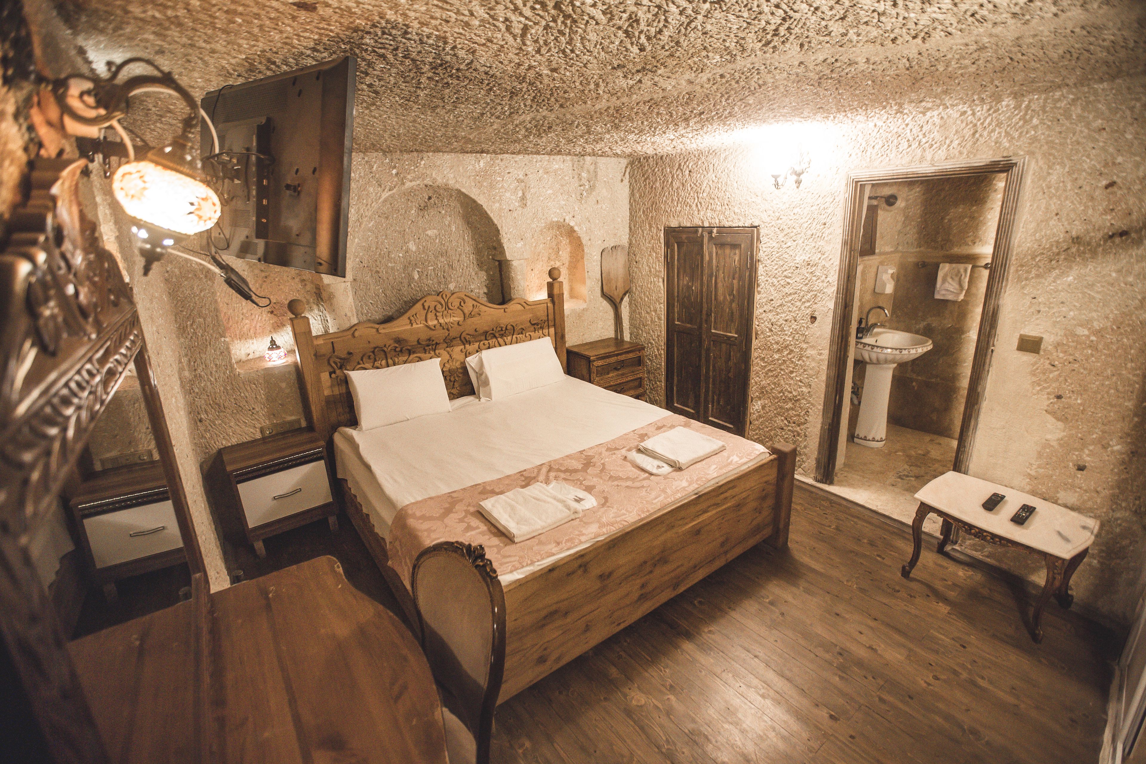 Une chambre rustique avec un lit en bois, des tables de chevet, un miroir, un banc en bois et une salle de bain équipée d’un lavabo et d’un miroir.