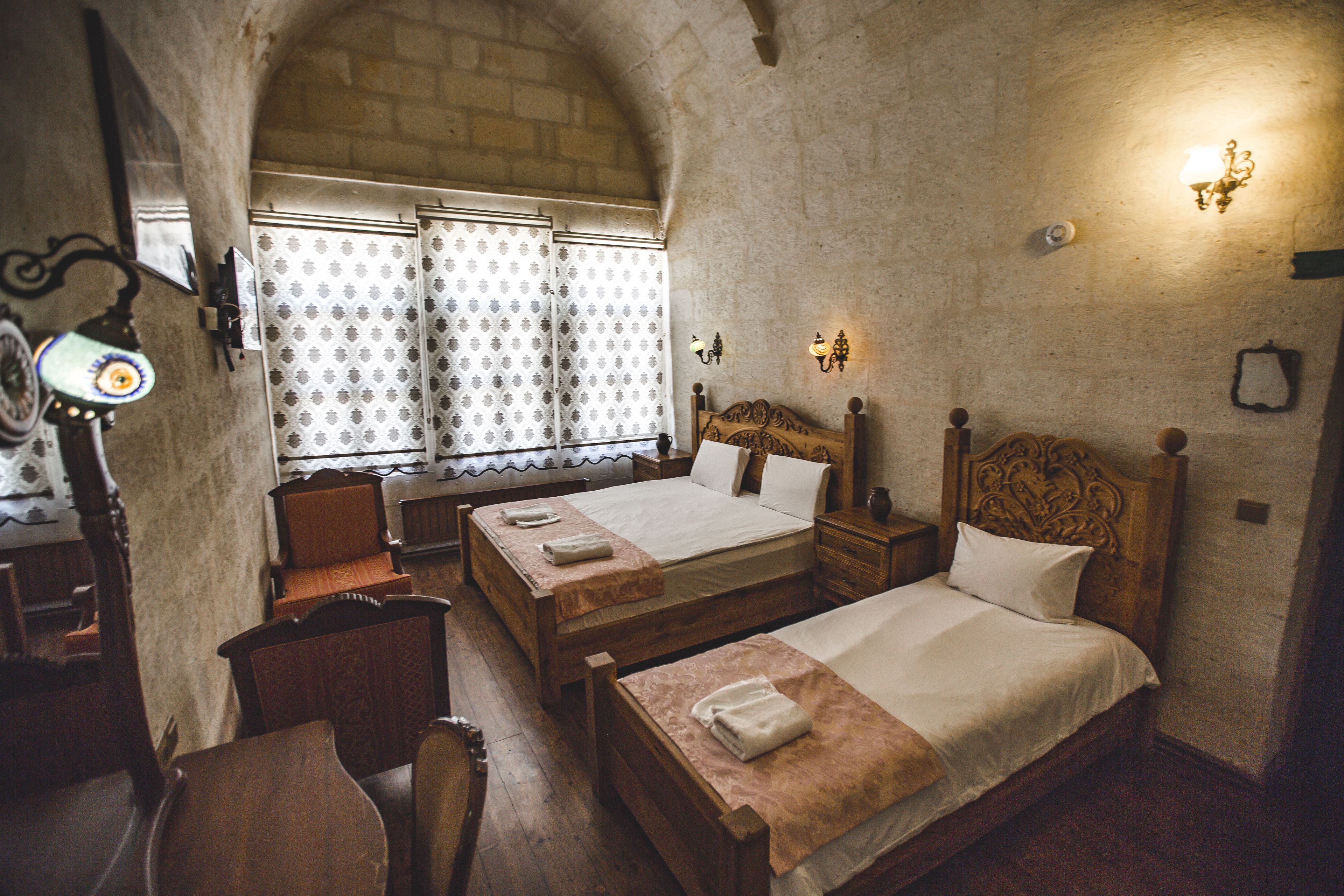 A traditional room with two wooden beds, a wooden chair, a small table, and a window with patterned curtains.
